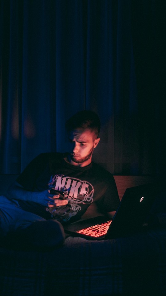 A young man working on a laptop in a dark room at night